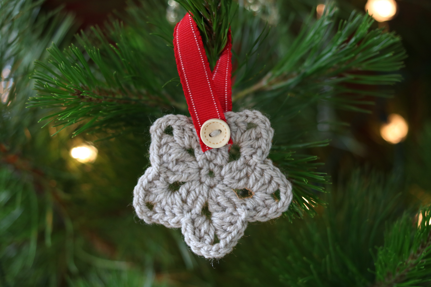 crochet Christmas star ornament in neutral colour with red ribbon & wood button