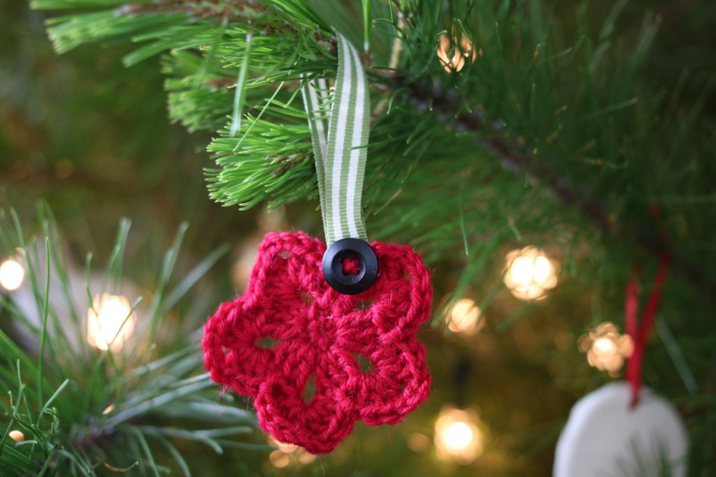 red wool crochet star ornament with green and white striped ribbon and black wooden hanging on a Christmas tree